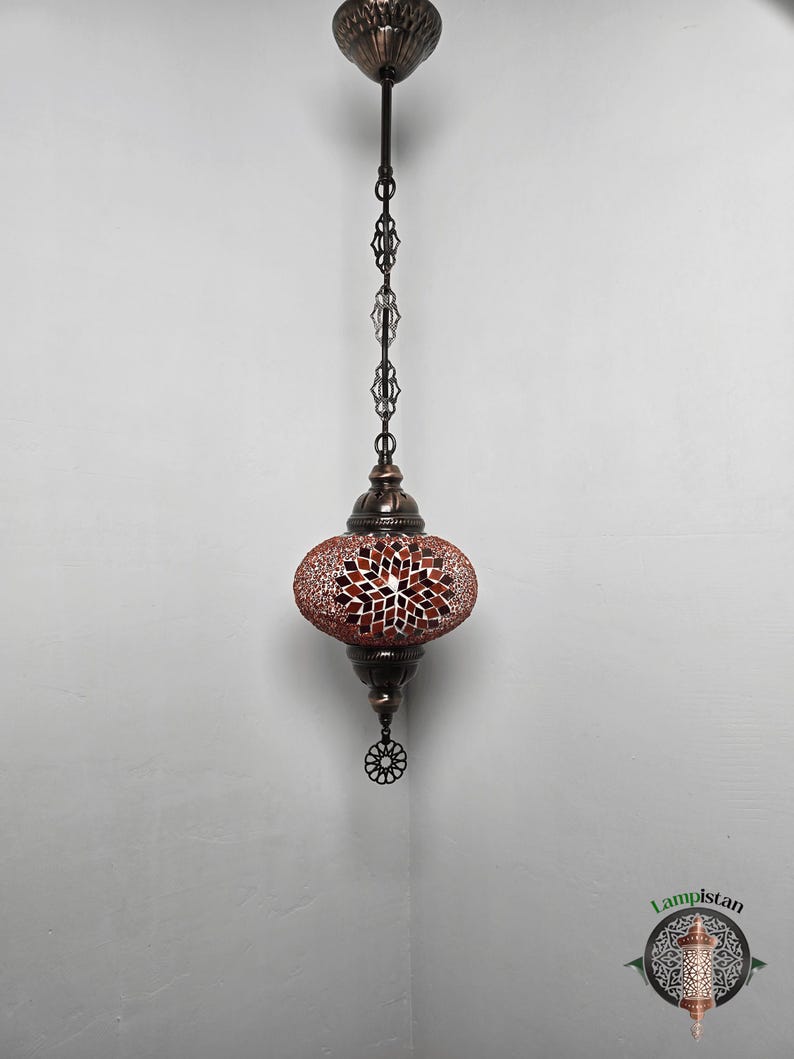 Op de afbeelding: Een hangende moza&iuml;ekglazen lamp met een rood en wit geometrisch patroon. De lamp heeft een zwarte metalen ketting en een decoratief metalen eindstuk.