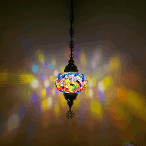 Op de afbeelding: Een kleurrijke moza&iuml;ek glazen hanglamp met een zwarte metalen ketting en een decoratief metalen eindstuk. Het licht werpt een kleurrijk patroon op het plafond.
