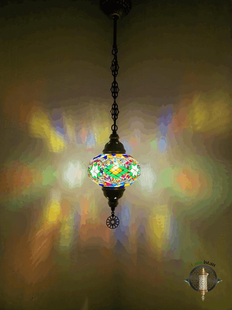Op de afbeelding: Een kleurrijke moza&iuml;ek glazen hanglamp hangt aan een ketting. Het licht werpt een regenboogpatroon op de muur.
