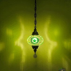 Op de afbeelding: Een groene en witte moza&iuml;ek glazen hanglamp met een zwarte metalen ketting en een decoratief metalen eindstuk. De lamp hangt aan een plafond.