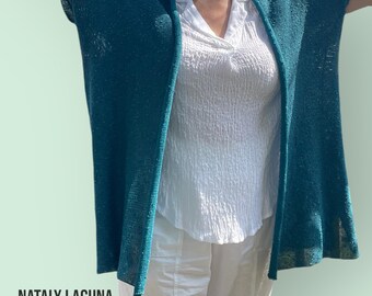 May include: A teal blue open-front cardigan with a loose fit. The cardigan is made of a lightweight, breathable fabric and has a relaxed, casual style.  The text "NATALY LAGUNA COTTON COLLECTION" is visible at the bottom of the image.