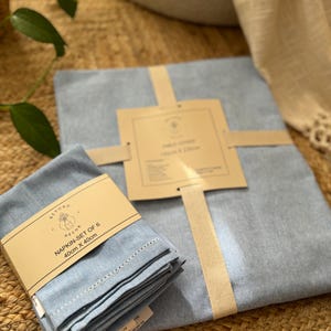 May include: A set of six blue linen napkins, 40cm x 40cm, packaged with a white ribbon and a brown label that reads "Napkin - Set of 6 40cm x 40cm" and "Beyond Decor".