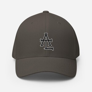 May include: A dark gray baseball cap with a curved brim. The cap features a black and white embroidered logo on the front. The logo is an ornate design of the letters "A" and "L".