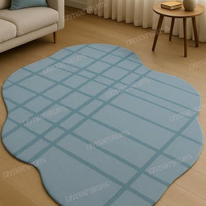 Könnte beinhalten: Hellblauer, unregelmäßig geformter Teppich mit einem Gittermuster in einem etwas dunkleren Blauton. Der Teppich liegt auf einem Holzboden. Der Raum umfasst auch ein Sofa, ein Kissen und einen Beistelltisch.