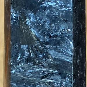 May include: A polished crystal tower with a pointed top, featuring a dark charcoal and black base color with intricate, shimmering silver and metallic gray needle-like inclusions throughout the stone, creating a textured, fibrous appearance.