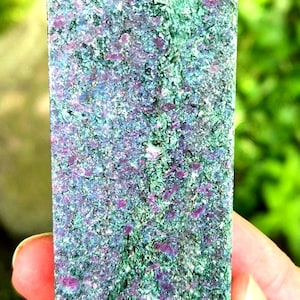 May include: A polished stone tower with a pointed top, featuring a mottled texture of deep green and vibrant magenta-pink mineral inclusions throughout the entire surface of the crystalline structure, displaying a natural variegated color pattern.