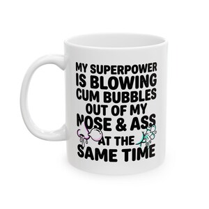 May include: A white ceramic mug featuring black text that reads: MY SUPERPOWER IS BLOWING CUM BUBBLES OUT OF MY NOSE & ASS AT THE SAME TIME. The design includes small, colourful illustrations of a nose and a rear end blowing bubbles.