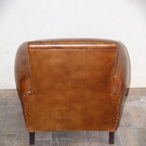 May include: A brown leather armchair with a rounded back and studded details. The chair has a simple design and is upholstered in a rich brown leather.
