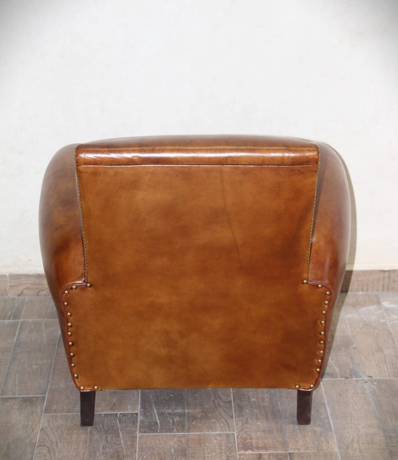 May include: A brown leather armchair with a rounded back and studded details. The chair has a simple design and is upholstered in a rich brown leather.