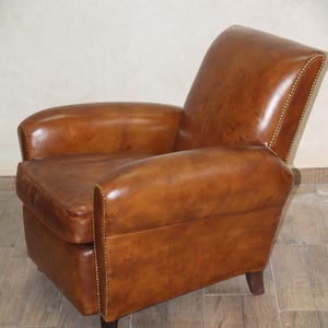 May include: A brown leather armchair with a tufted back and arms. The chair has a rounded shape and is accented with brass tacks.