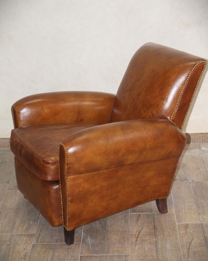 May include: A brown leather armchair with a tufted back and arms. The chair has a rounded shape and is accented with brass tacks.