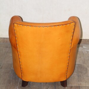 Pu&ograve; includere: Una poltrona in pelle marrone con schienale capitonn&eacute; e gambe in legno. La poltrona &egrave; rivestita in pelle color miele caldo e ha un design classico.