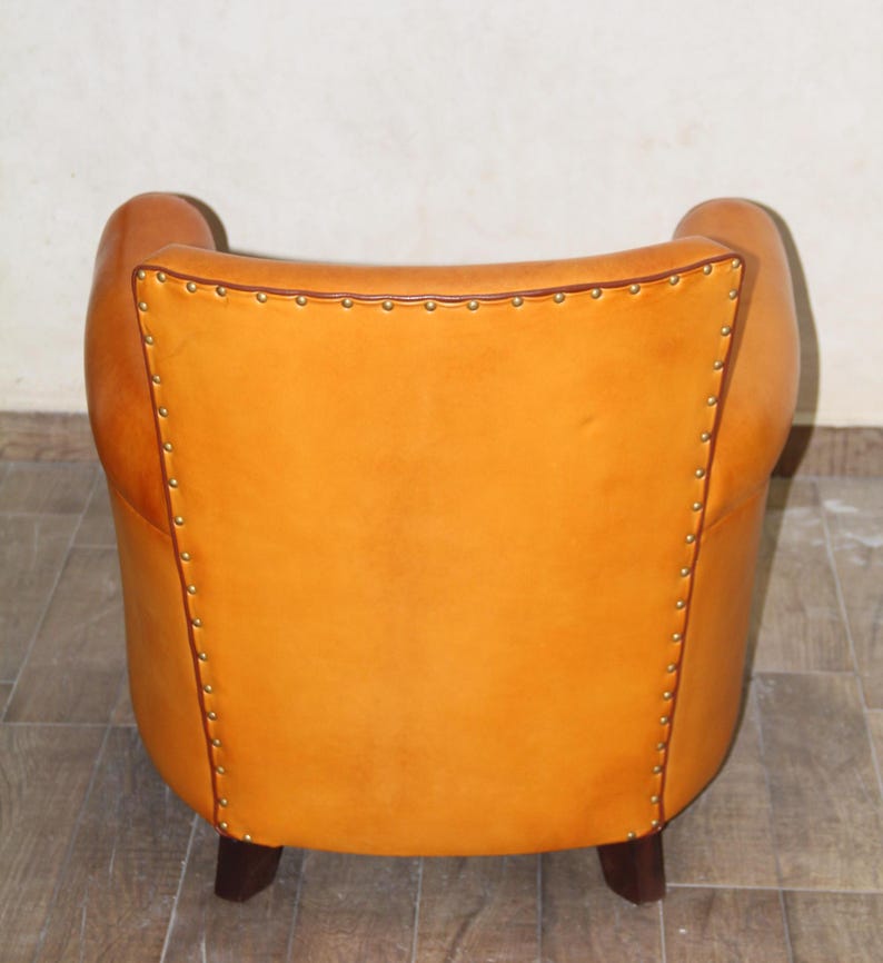 Pu&ograve; includere: Una poltrona in pelle marrone con schienale capitonn&eacute; e gambe in legno. La poltrona &egrave; rivestita in pelle color miele caldo e ha un design classico.