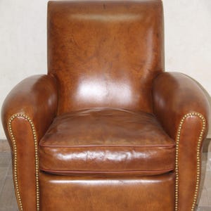 May include: A brown leather armchair with a tufted back and arms. The chair has a slightly distressed look and features brass nailhead trim.