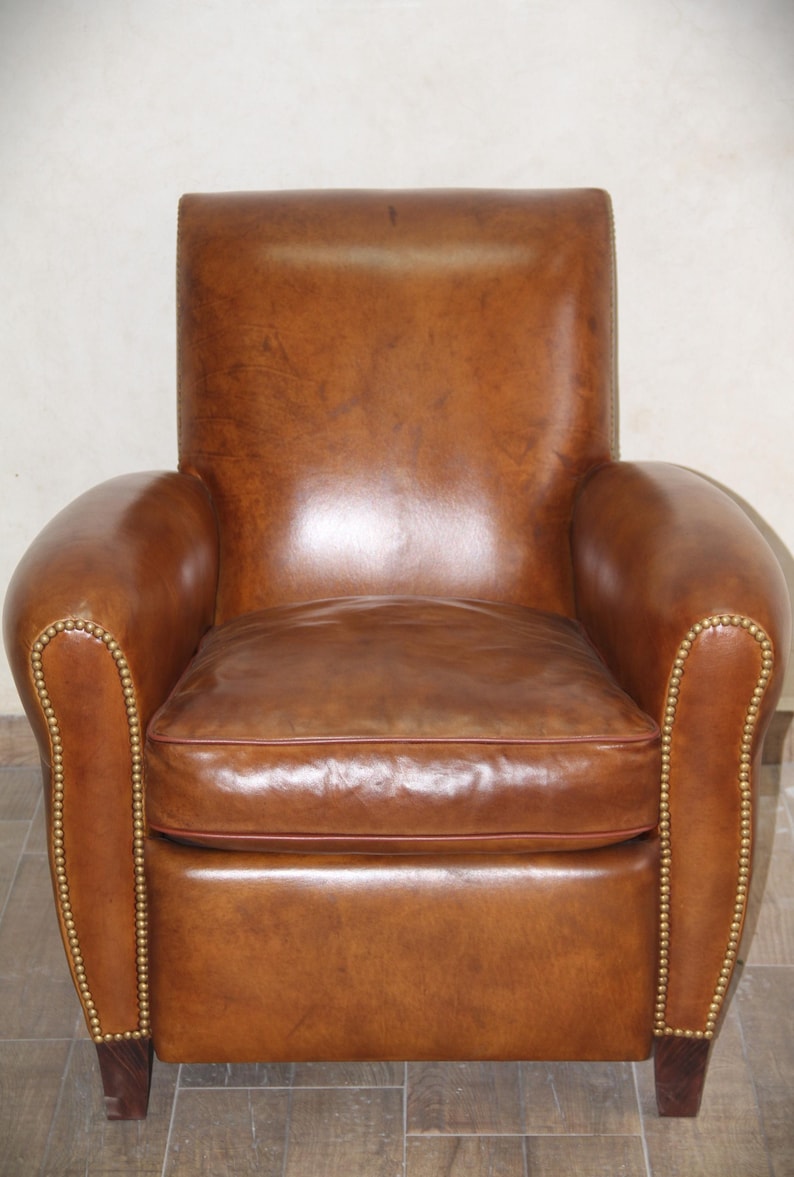 May include: A brown leather armchair with a tufted back and arms. The chair has a slightly distressed look and features brass nailhead trim.