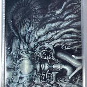 May include: A cassette tape with a dark, surreal illustration. The artwork features a detailed, grayscale depiction of a face with snake-like elements and intricate, flowing forms. The overall theme suggests a horror or fantasy genre.