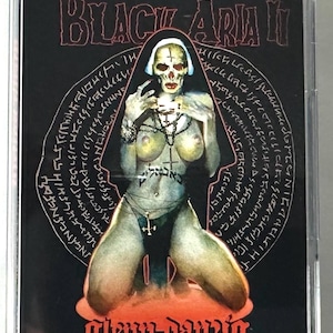 May include: A cassette tape with a black cover featuring the text "BLACK ARIA II" in red. The artwork depicts a skeletal figure with a cross, surrounded by an esoteric design. The artist's name, "Glenn Danzig," is at the bottom.