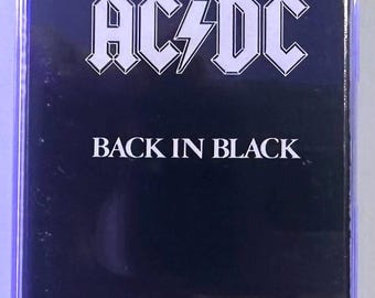 May include: A music cassette tape in a clear plastic case. The insert features a solid black background with the white AC/DC logo at the top and the text BACK IN BLACK printed in white capital letters centered below the band name.
