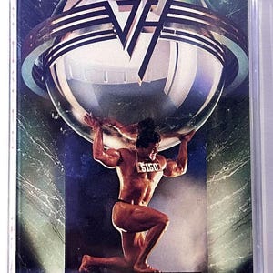 May include: A cassette tape featuring the band Van Halen. The cover art depicts a muscular figure kneeling and supporting a large, metallic sphere. The band's logo is above the sphere. The background has a blue and green gradient.