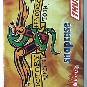 May include: A vintage, rectangular box with a colorful graphic design. The design features a stylized green snake-like creature with orange and black accents, and text that reads "18 Hardcore Tour" and "19 Victory Summer". The word "Thumb" is in a red box.