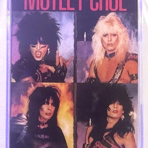 May include: A cassette tape featuring the band Mötley Crüe. The album cover has four images of the band members with long hair and makeup. The album title "Shout at the Devil" is printed at the bottom in white text.