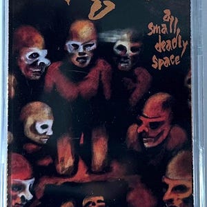 May include: A cassette tape case featuring the album art for "Fight - Small Deadly Space." The artwork depicts a group of figures with skull-like faces in shades of red, brown, and white against a dark background. The word "Fight" is at the top.