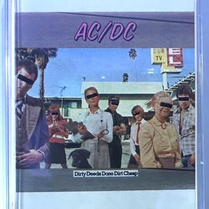 May include: A vintage cassette tape featuring the album art for AC/DC's "Dirty Deeds Done Dirt Cheap." The cover art depicts a group of people with black bars over their eyes. The band's name is in pink letters.