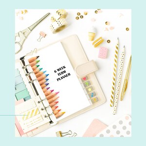 May include: A white planner with the text "6 Week Term Planner" on the cover. The planner is surrounded by colorful pencils, washi tape, and other stationery supplies.