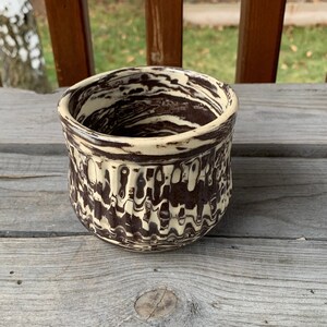 May include: A ceramic mug with a brown and white marbled glaze. The mug has a textured, wavy design.