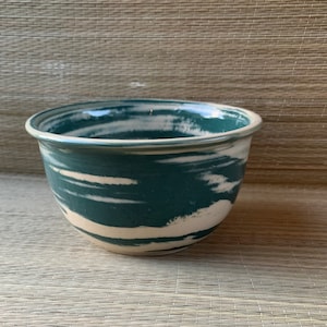 May include: A teal and white ceramic bowl with a swirling pattern. The bowl is round and has a smooth, glazed finish.