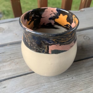 May include: A ceramic vase with a white base and a black, pink, and gold marbled rim.