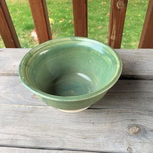 May include: A green ceramic bowl with a white rim. The bowl is glazed with a light green and blue color.