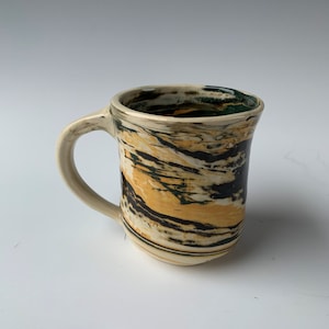 May include: A ceramic mug with a white base and a swirling pattern of black, yellow, and green glaze.