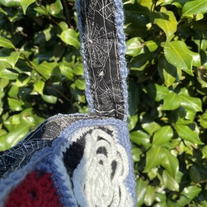 May include: A crocheted bag with a red, blue and white design. The bag has a black and white spiderweb fabric lining.