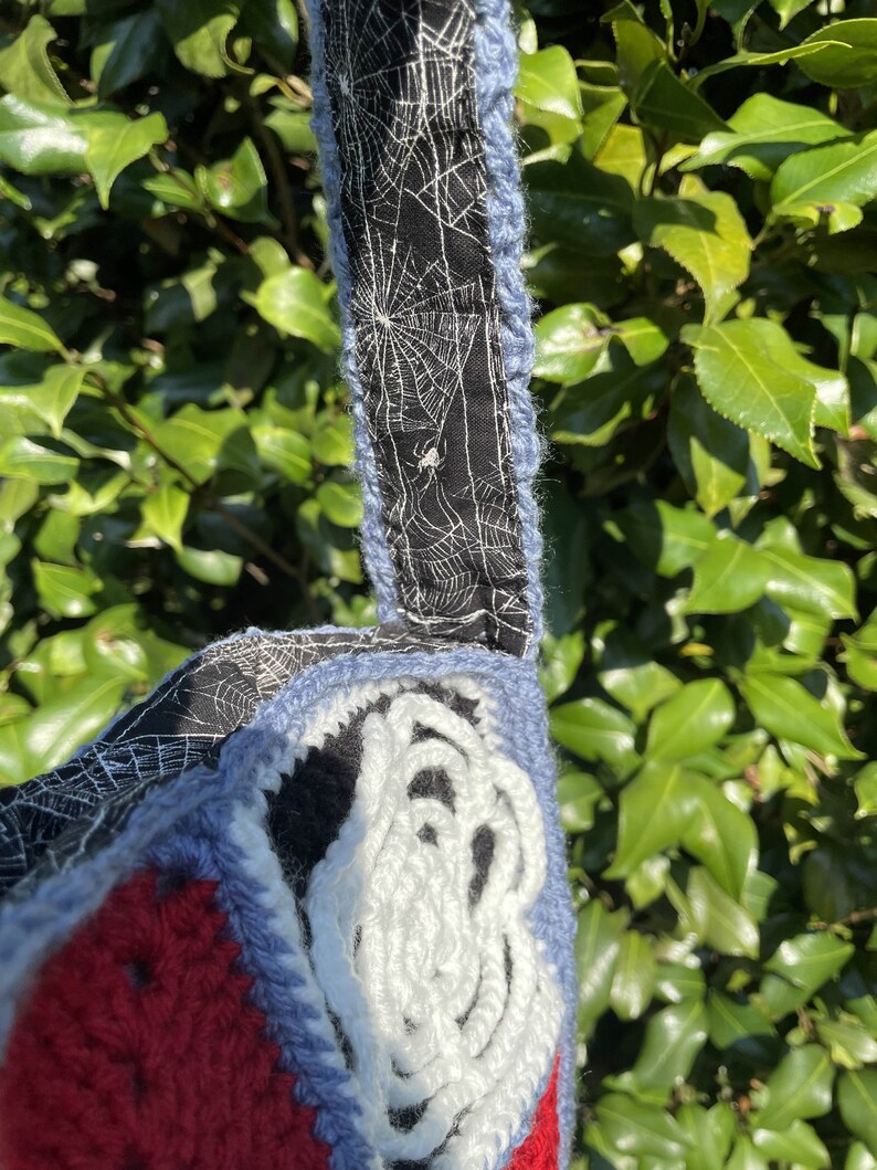 May include: A crocheted bag with a red, blue and white design. The bag has a black and white spiderweb fabric lining.