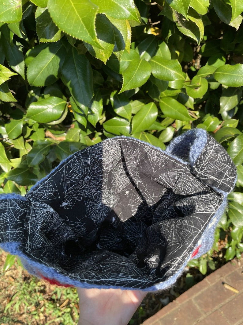 May include: Blue knitted bag with a spiderweb pattern lining. The bag is made of soft yarn and has a fluffy texture.