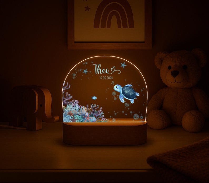 K&ouml;nnte beinhalten: Ein halbkreisf&ouml;rmiges Acryl-Nachtlicht mit einer farbenfrohen Unterwasserszene, die eine Meeresschildkr&ouml;te, ein Korallenriff und Blasen zeigt. Das Licht ist mit dem Namen Theo und dem Datum 16.05.2024 auf einem Holzsockel personalisiert.