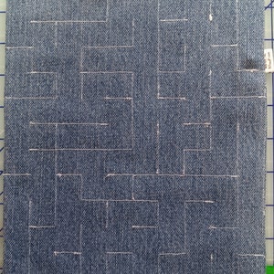 Pode incluir: Um tecido de ganga azul com um padrão branco de quadrados e retângulos costurados.