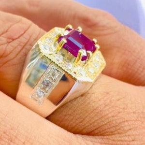 May include: A gold and silver ring with a large, square-cut ruby gemstone surrounded by smaller diamonds. The ring has a thick band and a detailed design.