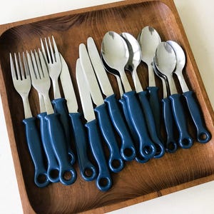 May include: A set of stainless steel silverware with navy blue handles, including forks, knives, and spoons, arranged in a wooden tray. The silverware is designed for multiple place settings.