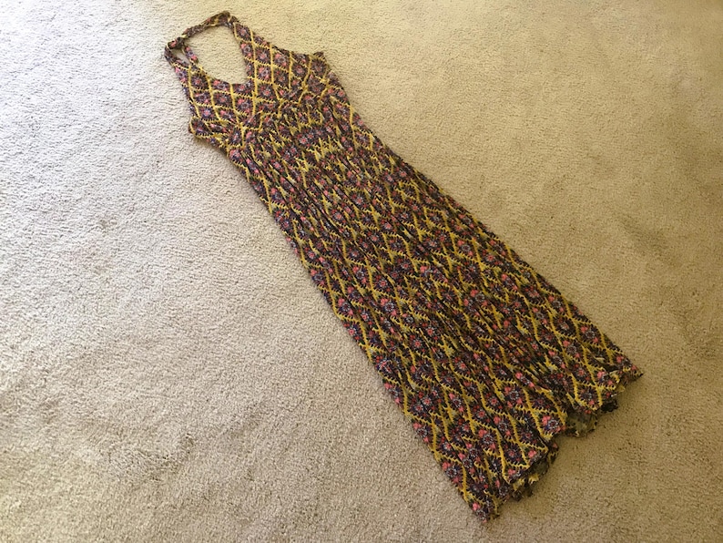 Op de afbeelding: Een maxi-jurk met halternek met een geometrisch patroon in geel, bruin en roze. De jurk is gemaakt van een lichte stof en heeft een vloeiend silhouet. De jurk is ongeveer 140 cm lang.