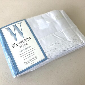 May include: A white twin sheet set by Wamsutta Soft & Easy in plastic packaging. The set features a decorative eyelet lace trim along the edge. The label displays the Wamsutta logo, 250 thread count, and states the material is 50% cotton and 50% polyester.