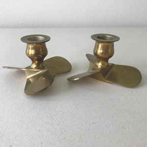 Puede incluir: Dos candelabros de metal dorado con forma de h&eacute;lice. Cada candelabro tiene una parte superior redonda con un peque&ntilde;o borde para sujetar una vela.