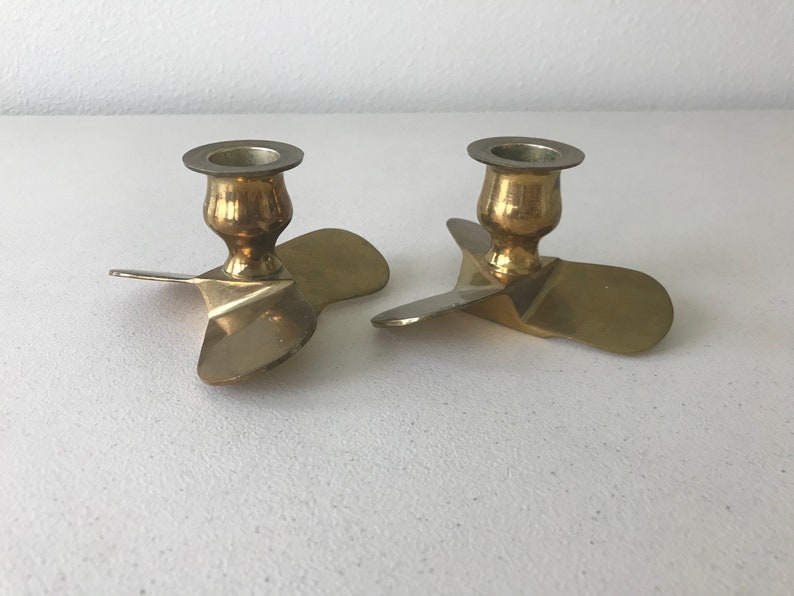 Puede incluir: Dos candelabros de metal dorado con forma de h&eacute;lice. Cada candelabro tiene una parte superior redonda con un peque&ntilde;o borde para sujetar una vela.