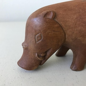 K&ouml;nnte beinhalten: Eine Holzskulptur eines Warzenschweins. Die braune Figur hat detaillierte Merkmale, darunter eine rautenf&ouml;rmige Markierung auf der Stirn und Sto&szlig;z&auml;hne. Das Warzenschwein wird in einer Laufpose dargestellt.