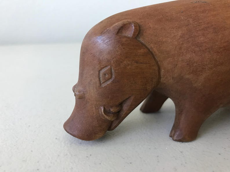 K&ouml;nnte beinhalten: Eine Holzskulptur eines Warzenschweins. Die braune Figur hat detaillierte Merkmale, darunter eine rautenf&ouml;rmige Markierung auf der Stirn und Sto&szlig;z&auml;hne. Das Warzenschwein wird in einer Laufpose dargestellt.