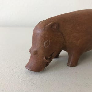 K&ouml;nnte beinhalten: Eine handgeschnitzte Holzfigur eines Flusspferds. Das Flusspferd ist braun mit glatter Oberfl&auml;che und steht auf vier Beinen, der Kopf gesenkt. Die Figur hat geschnitzte Details, darunter eine rautenf&ouml;rmige Markierung auf der Stirn.
