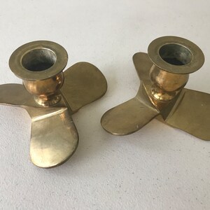 Puede incluir: Dos candelabros de metal dorado con forma de h&eacute;lice. Cada candelabro tiene tres aspas y una parte superior redonda para sujetar una vela.