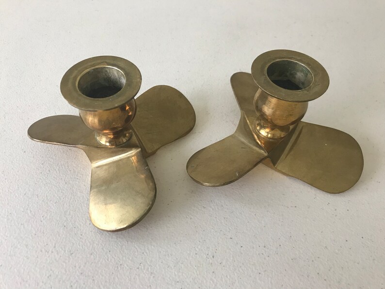 Puede incluir: Dos candelabros de metal dorado con forma de h&eacute;lice. Cada candelabro tiene tres aspas y una parte superior redonda para sujetar una vela.