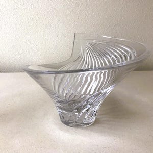 Pode incluir: Tigela decorativa de vidro transparente com uma forma assim&eacute;trica incomum. A tigela apresenta um padr&atilde;o de redemoinho e texturizado no exterior, criando um efeito visual din&acirc;mico. O design &eacute; elegante e moderno, adequado para exibi&ccedil;&atilde;o ou servir.